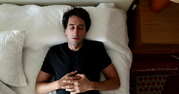 Pensive young man lying in bed resting. Thoughtful person lies in bed in thought