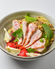 Fresh salad with chicken breast, cheese and tomatoes. Served in a bowl over white background.