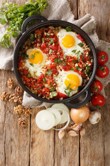 Georgian breakfast fried eggs with tomatoes, onions and walnuts close-up in a frying pan on the table. vertical top view from above