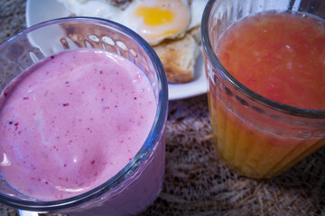 A berry smoothie and a glass of grapefruit juice with an egg in the background for breakfast.