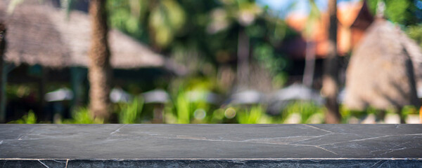 Empty black marble stone table top and blurred green tree and tropical garden in resort background...