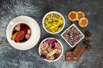 close up view of herbal tea with dry flowers and cookies and chocolate bars and anise on grey ground