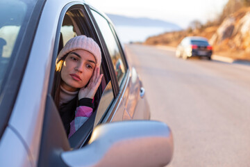 A woman with a winter hat is driving on a mountain and looking in the rearview mirror.