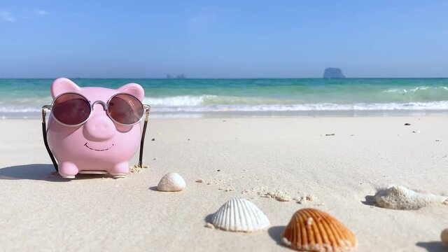 Piggy bank in summer vacation, going to beach and sea sand background. Saving money for holiday travel to south Thailand sea. Beautiful  sunny blue sky and ocean waves background screen