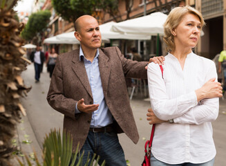 irritated senior woman standing back to man trying to talk outdoors