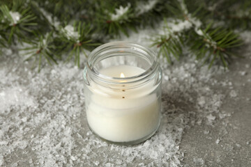 Fototapeta na wymiar Scented candle, pine branches and snow on gray background