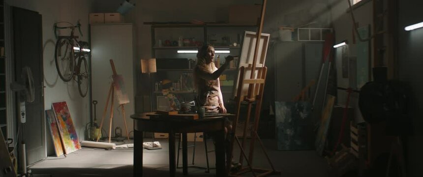 WIDE Female artist working on a new painting in her home garage studio. Remembering old hobbies during COVID-19 isolation. Shot with 2x anamorphic lens