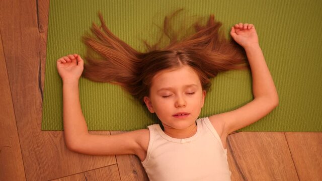 Cute little child girl lying on the floor and green yoga mat pretending to be asleep for fun