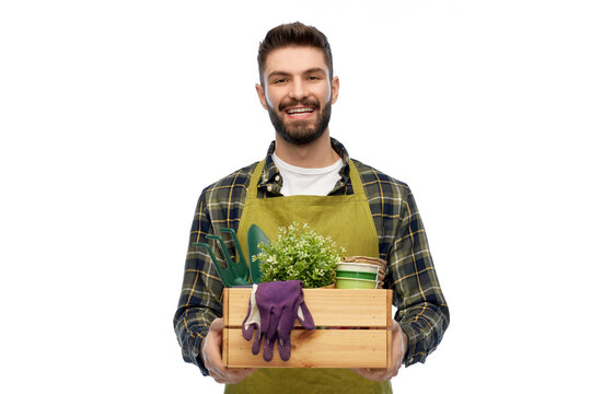 gardening, farming and people concept - happy smiling male gardener or farmer in apron with box of garden tools over white background