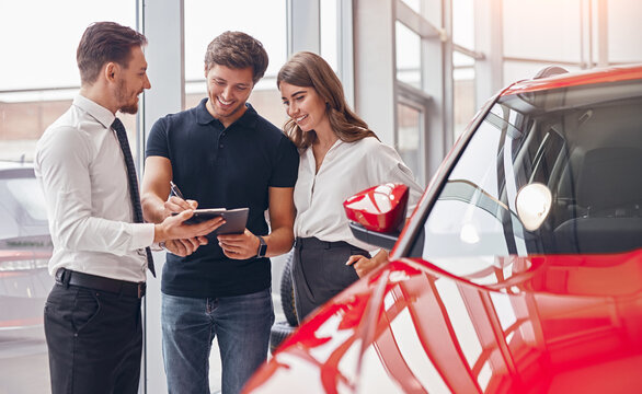Delighted couple and manager signing papers in car dealership