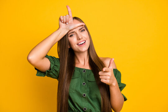 Portrait of pretty cheerful brown-haired girl bullying pointing at you showing horn sign isolated over bright yellow color background