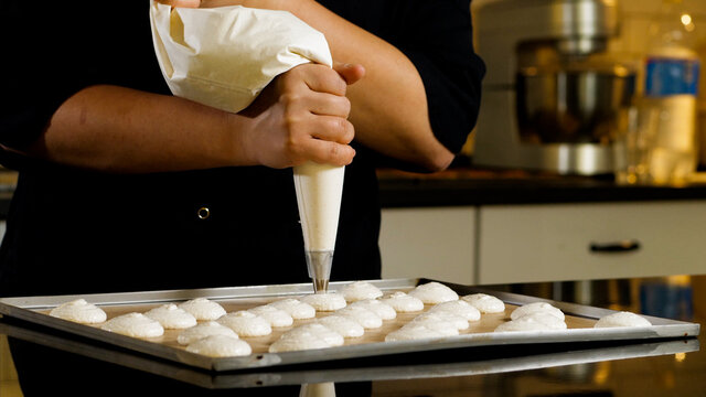 Chef making base for preparation macaron dessert. Close-up of extruding white creme from piping bag on metal tray for baking base of macaron dessert.