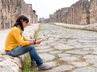Fototapeta premium Side view of a woman in yellow clothes sitting while checking tourist map of ancient ruins
