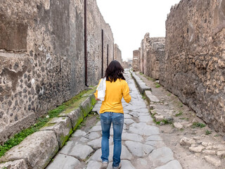 Fototapeta premium Rear view of a woman in yellow clothes walking while exploring ancient ruins