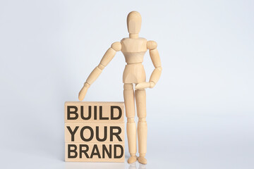 Wooden man shows with a hand text BUILD YOUR BRAND concept on the wooden block