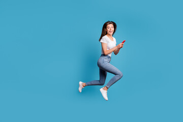 Fototapeta na wymiar Full body profile side photo of shocked student run jump copyspace wear casual outfit hold phone isolated on blue color background