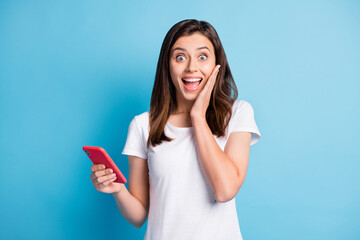 Naklejka premium Photo of young happy shocked amazed crazy girl hold smartphone sees unbelievable news isolated on blue color background