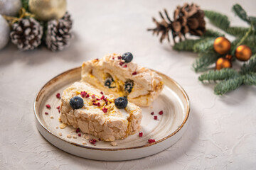 Two pieces of meringue roll cake with cream, berries and almond on plate, selective focus, in the background Christmas tree branches with cones and toys