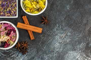 cinnamon sticks with three bowls of dry flower and anise on the left side of grey ground