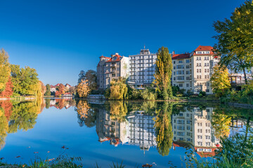 Fototapeta na wymiar Park at the shore of Lake Lietzen with buildings reflecting in the water in Berlin, Germany