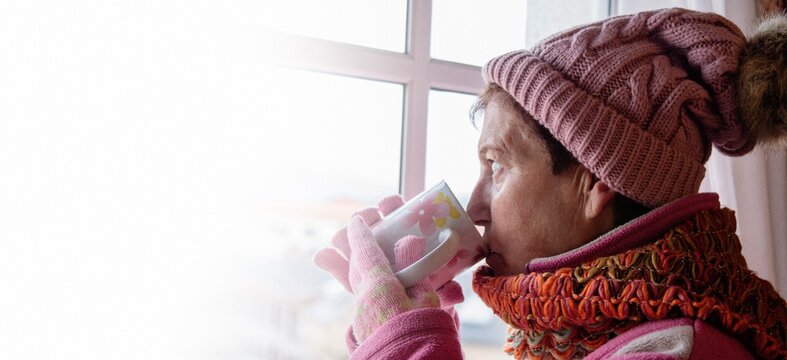 Cold Senior Woman With Cup Looking Out The Window