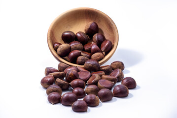Chestnuts spilled from wooden bowl on white background. Castanea sativa, sweet ripe Chestnuts