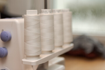 Fototapeta na wymiar Detail of four thread spools with white thread on overlock sewing machine