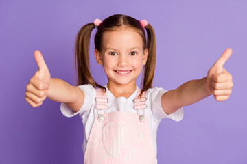 Photo of happy little girl make two thumbs up charming smile recommend isolated on purple color...