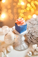 Mini mousse pastry dessert with blue velour. garland lamps bokeh background. In the form of gift box, ribbons of chocolate. Modern european cake. French cuisine. Christmas theme