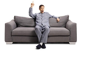 Young man in pajamas seated on a sofa pointing up
