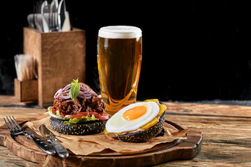 Set of hamburger with egg and beer. A standard set of drinks and food in the pub, beer and snacks. Dark background, fast food. Traditional american food.