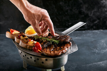 Grilled meat platter. Assorted delicious grilled meat with vegetables. Grilled mixed meat with pepper sauce and vegetables. Chef's hands spread meat on a plate