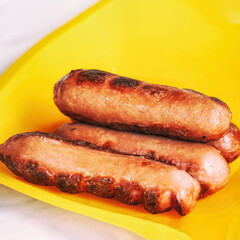 Grilled sausages on a yellow plastic plate
