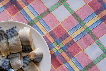 Pieces of fresh and delicious homemade pickled herring on a plate close-up. A plate of herring on the table with a checkered tablecloth.