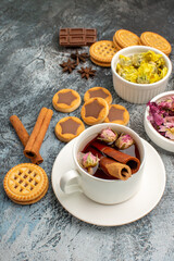 sidewise shot of a cup of herbal tea with cookies and cinnamons and dry flowers on grey background