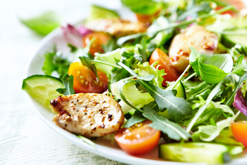 Salad with Chicken Breast, Cherry Tomatoes, Cucumber, Rocket and fresh Basil. Bright wooden background. Close up. 