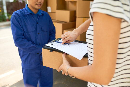 Cropped image of courier asking female customer to sign delivery service document