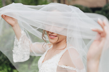 A smiling, sweet bride holds a veil with her hands and looks out from under it. Wedding close-up...