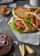 Lavash salad with fried chicken and vegetables. Pita with chicken nuggets, tomatoes, red onions and lettuce and sauce. Healthy fast food. Dark background. Vertical view