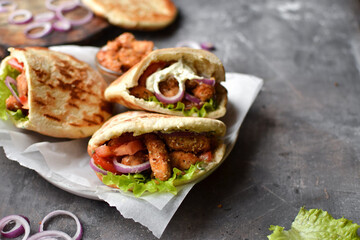 Lavash salad with fried chicken and vegetables. Pita with chicken nuggets, tomatoes, red onions and lettuce and sauce. Healthy fast food. Dark background. Copyspace