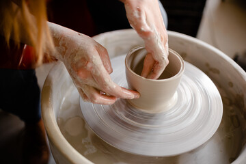 Female hands crafting a pottery cup on a potter's wheel. Handmade and crafting concept.