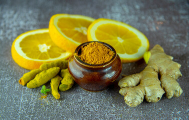 Dry turmeric root, turmeric powder, ginger and citrus on a wooden surface.