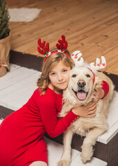 Blonde teenager and her dog with antlers on their heads are hugging on the steps