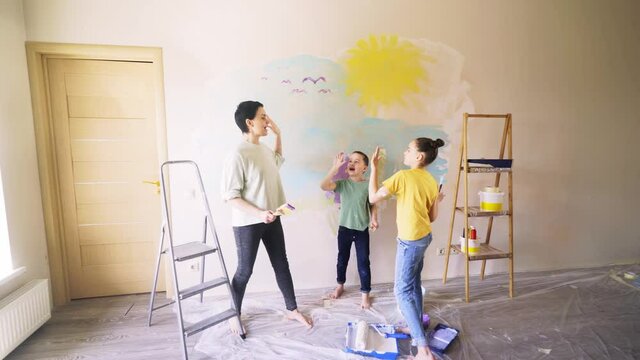 Family give five to each other, cheerful mother helps children to painting flat wall after relocation drawing images for kids birthday on holiday or isolation