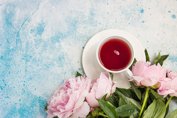 Cup of tea and pink peonies flowers on blue background. Top view with copy space for text. Present for Woman or Mother day.