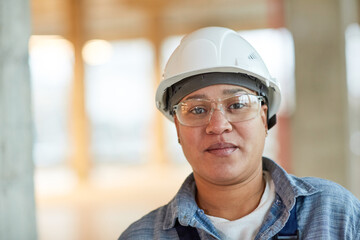 Front view portrait of female worker wearing hardhat and looking at camera while standing on construction site, copy space