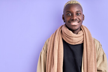 fancy black guy in beige coat posing at camera isolated over violet purple background in studio. young male with stylish haircut looks at camera and smiles