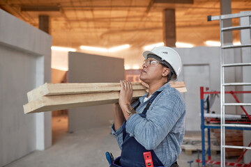 Waist up portrait of modern female worker carrying wood boards while working on construction site, copy space