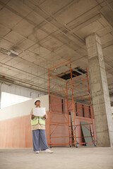 Vertical wide angle portrait of contemporary female engineer looking at documents while standing on construction site, copy space