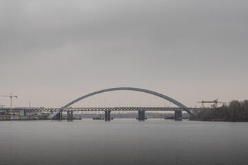 Fototapeta na wymiar Arch bridge on Podil over the river Dnieper in the city of Kiev, on a cloudy day in autumn, at the last stage of construction, side view.